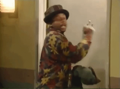 A Man Wearing A Hat And A Floral Shirt Is Standing In Front Of A Door And Giving The Middle Finger . GIF