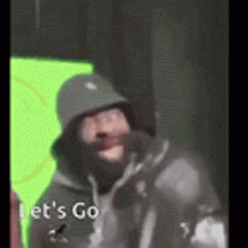 A Man Wearing A Hat And A Hoodie Is Standing In Front Of A Green Screen . GIF