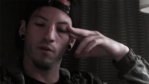 A Man Wearing A Hat And A Jacket Is Holding His Hand To His Forehead . GIF