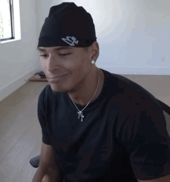 A Man Wearing A Hat And A Necklace Is Smiling GIF