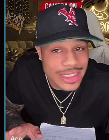 A Man Wearing A Hat And A Necklace Is Smiling GIF