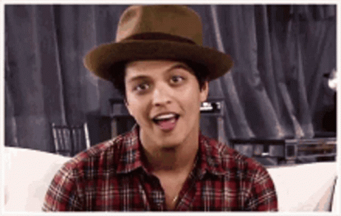 A Man Wearing A Hat And A Plaid Shirt Is Sitting On A Couch And Making A Funny Face . GIF