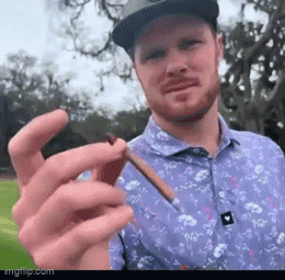 a man wearing a hat and a purple shirt is holding a cigarette in his hand .