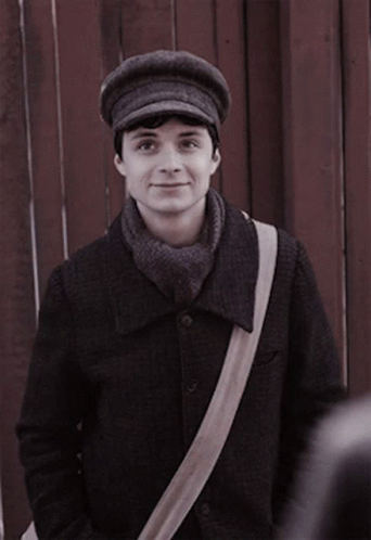 A Man Wearing A Hat And A Scarf Is Standing In Front Of A Wooden Fence GIF