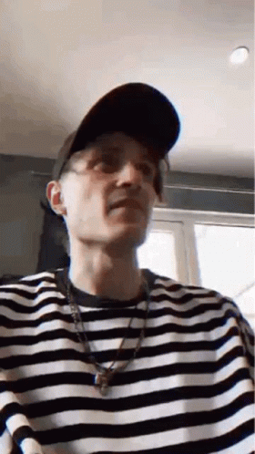 A Man Wearing A Hat And A Striped Shirt Is Making A Face . GIF