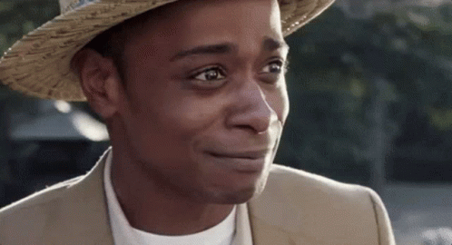 A Man Wearing A Hat And A Suit Is Smiling And Looking At The Camera . GIF