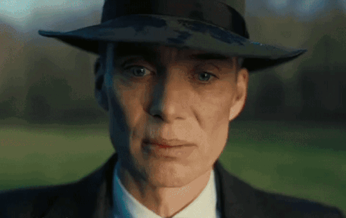 A Man Wearing A Hat And A Suit Looks At The Camera GIF