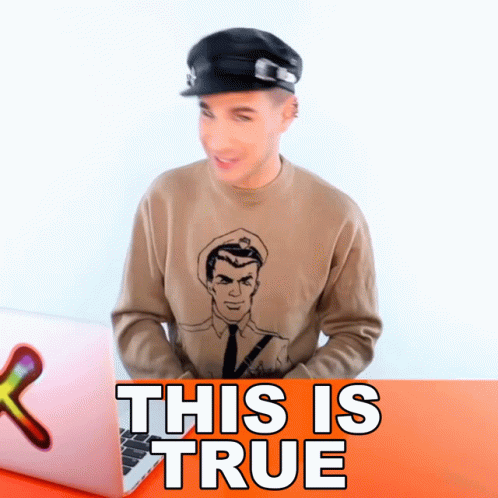 A Man Wearing A Hat And A Sweater That Says This Is True Sits In Front Of A Laptop GIF
