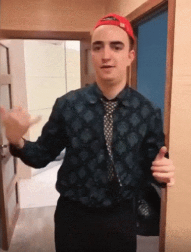 A Man Wearing A Hat And A Tie Is Standing In A Doorway GIF