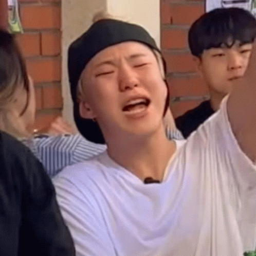 A Man Wearing A Hat And A White Shirt Is Making A Funny Face While Sitting In A Crowd . GIF