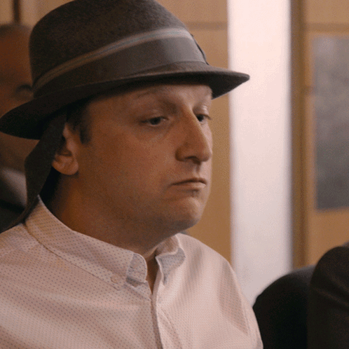 A Man Wearing A Hat And A White Shirt Looks To The Side GIF
