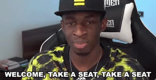 A Man Wearing A Hat And A Yellow Shirt Is Sitting In A Chair And Making A Funny Face . GIF