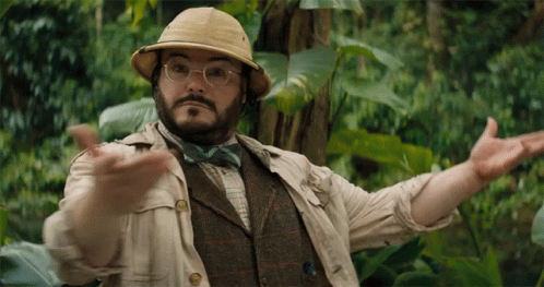 A Man Wearing A Hat And Bow Tie Is Standing In The Jungle GIF