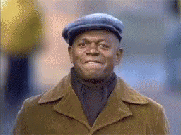 A Man Wearing A Hat And Coat Is Smiling . GIF