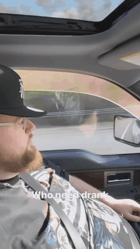 A Man Wearing A Hat And Glasses Is Driving A Car With The Words Who Needs Drank Below Him GIF