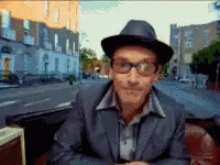 a man wearing a hat and glasses is sitting in front of a city street