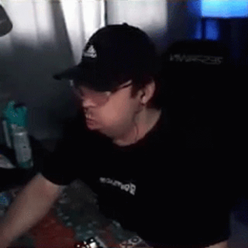 A Man Wearing A Hat And Glasses Is Sitting In Front Of A Computer . GIF