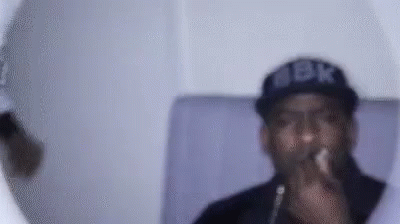 A Man Wearing A Hat And Glasses Is Smoking A Cigarette . GIF