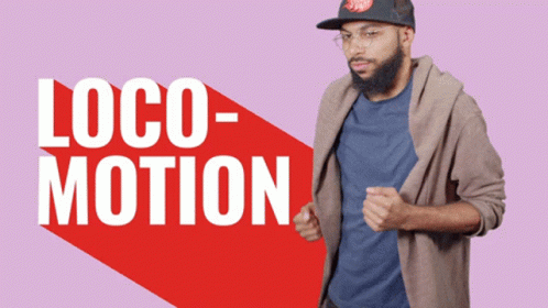 A Man Wearing A Hat And Glasses Is Standing In Front Of A Sign That Says Loco Motion GIF