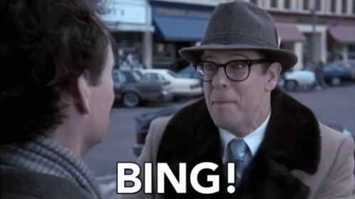 A Man Wearing A Hat And Glasses Is Talking To Another Man On A City Street . GIF