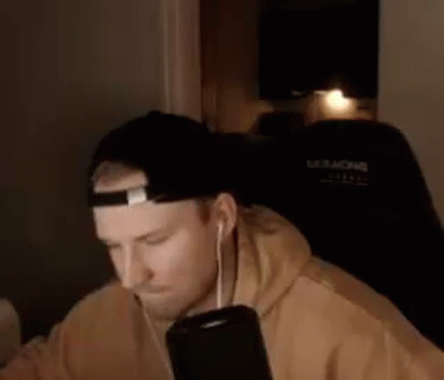 A Man Wearing A Hat And Headphones Is Sitting In A Chair . GIF
