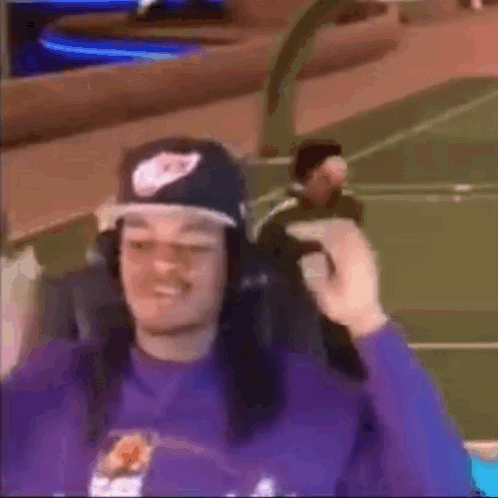 A Man Wearing A Hat And Headphones Is Sitting In A Chair On A Basketball Court . GIF