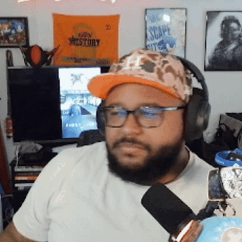 A Man Wearing A Hat And Headphones Is Sitting In Front Of A Sign That Says Escape Kit GIF