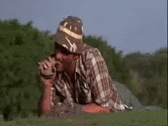 A Man Wearing A Hat And Sunglasses Is Laying Down In The Grass . GIF
