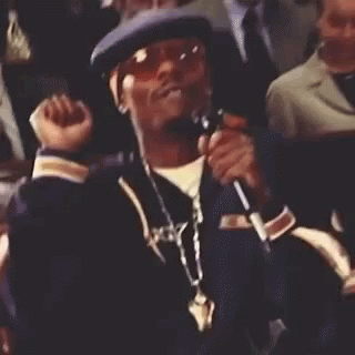 A Man Wearing A Hat And Sunglasses Is Sitting In A Crowd And Smiling . GIF