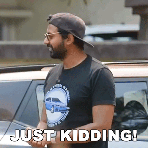 A Man Wearing A Hat And Sunglasses Is Standing In Front Of A Car And Says Just Kidding ! GIF