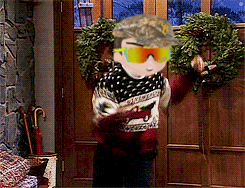 A Man Wearing A Hat And Sunglasses Is Standing In Front Of A Door With A Wreath On It GIF