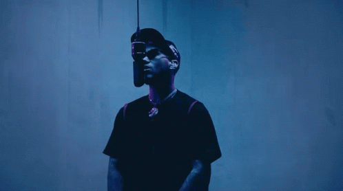 A Man Wearing A Hat And Sunglasses Is Standing In Front Of A Microphone GIF