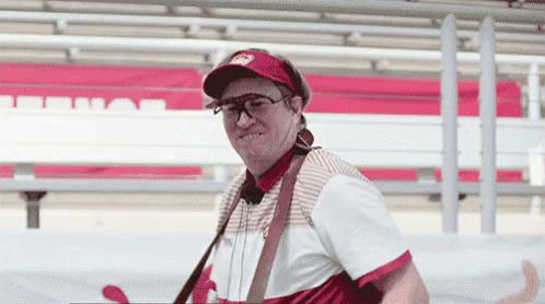 A Man Wearing A Hat And Sunglasses Is Standing In Front Of A Red And White Bench . GIF