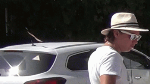 A Man Wearing A Hat And Sunglasses Is Standing In Front Of A White Suv . GIF