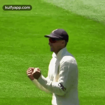 A Man Wearing A Hat And Sunglasses Is Standing On A Cricket Field . GIF