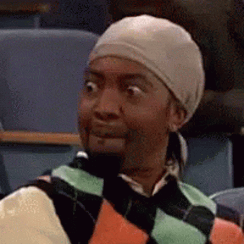 A Man Wearing A Hat And Sweater Is Sitting In A Classroom . GIF
