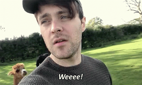 A Man Wearing A Hat And Sweater Says Weeeee While Standing In A Field GIF