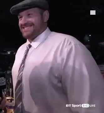 A Man Wearing A Hat And Tie Is Smiling And Holding A Glass Of Beer . GIF