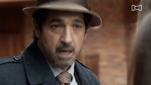 A Man Wearing A Hat And Tie Is Talking To Another Man GIF
