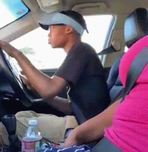 A Man Wearing A Hat And Visor Is Driving A Car Next To A Woman In A Pink Shirt GIF