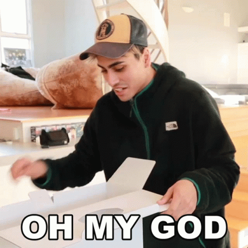 A Man Wearing A Hat Is Opening A Box With The Words Oh My God On The Bottom GIF