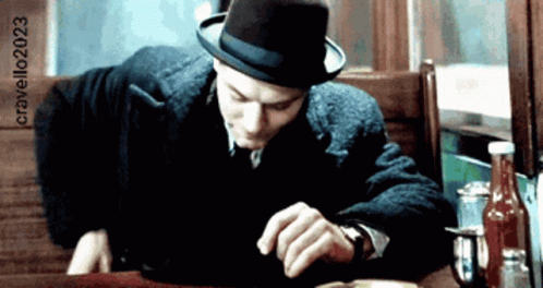 A Man Wearing A Hat Is Sitting At A Table With A Bottle Of Ketchup In The Foreground GIF