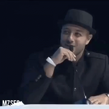 A Man Wearing A Hat Is Sitting At A Table With A Microphone In Front Of Him . GIF