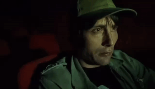A Man Wearing A Hat Is Sitting In A Dark Room . GIF