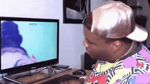 a man wearing a hat is sitting in front of a computer screen