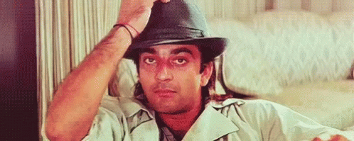A Man Wearing A Hat Is Sitting On A Couch And Adjusting His Hat . GIF