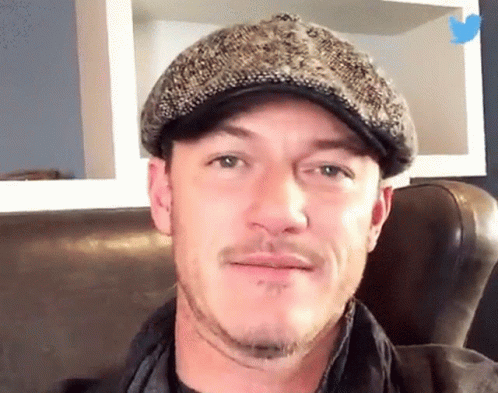 A Man Wearing A Hat Is Sitting On A Couch And Smiling GIF