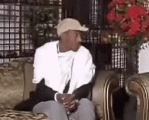 A Man Wearing A Hat Is Sitting On A Couch . GIF