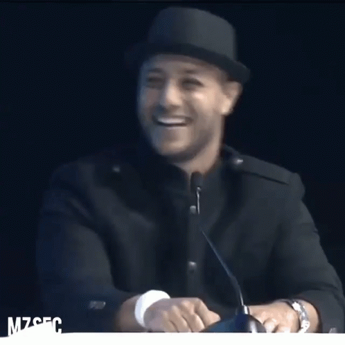 A Man Wearing A Hat Is Smiling In Front Of A Microphone With The Letters Mzsfc On The Bottom GIF