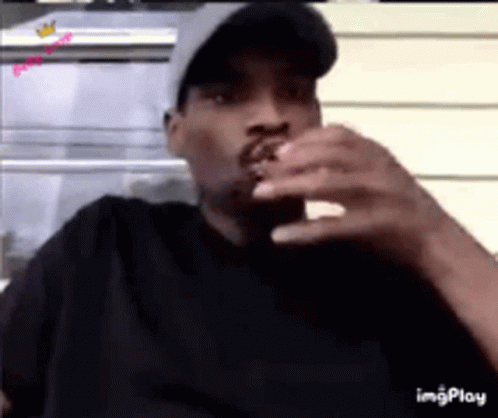 A Man Wearing A Hat Is Smoking A Cigarette While Looking At His Phone . GIF